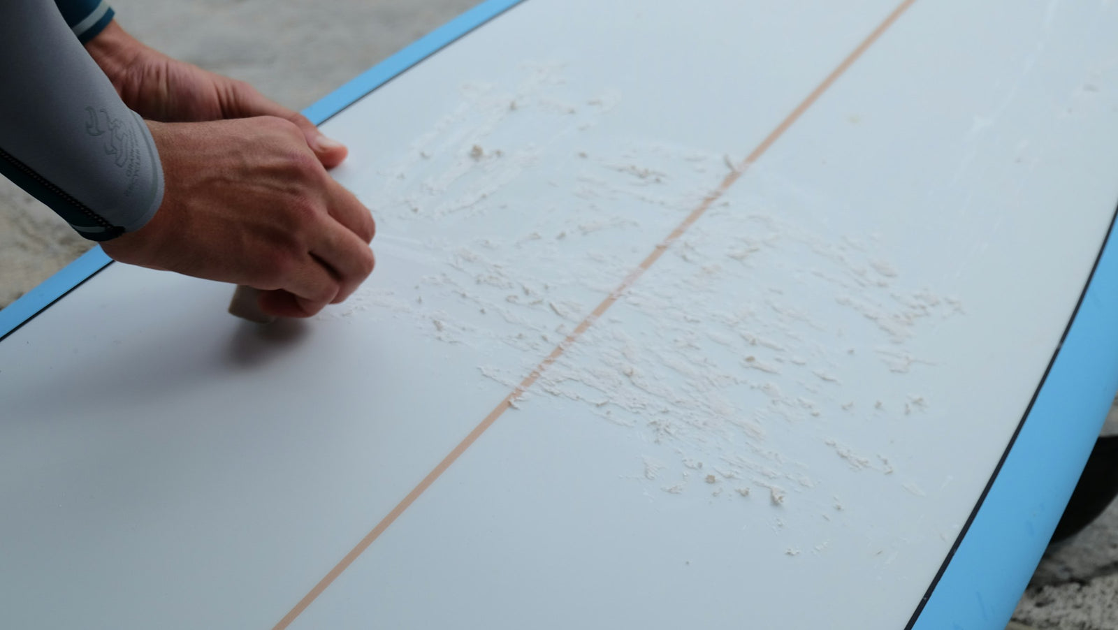 A hand waxing the deck of a surfboard